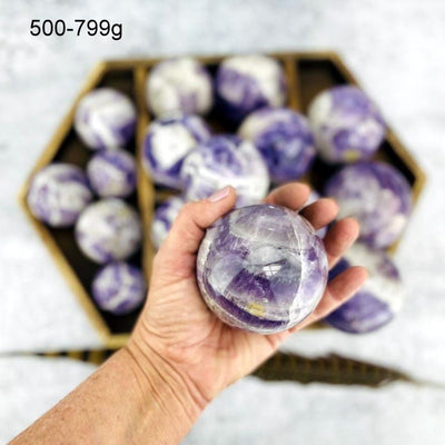 Chevron Amethyst Polished Sphere of 500-799g displayed in palm of woman's hand.