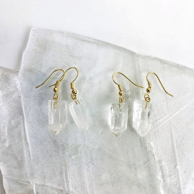 Close up of two pairs of crystal point earrings in gold plated on a selenite slab.