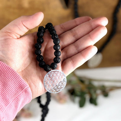 Diffuser Necklace Lava Bead with Flower of Life Charm in Silver in Hand on White Background.