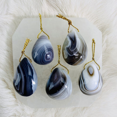 Picture of 5 of our agate tumbled pendants displayed on a selenite charging plate.