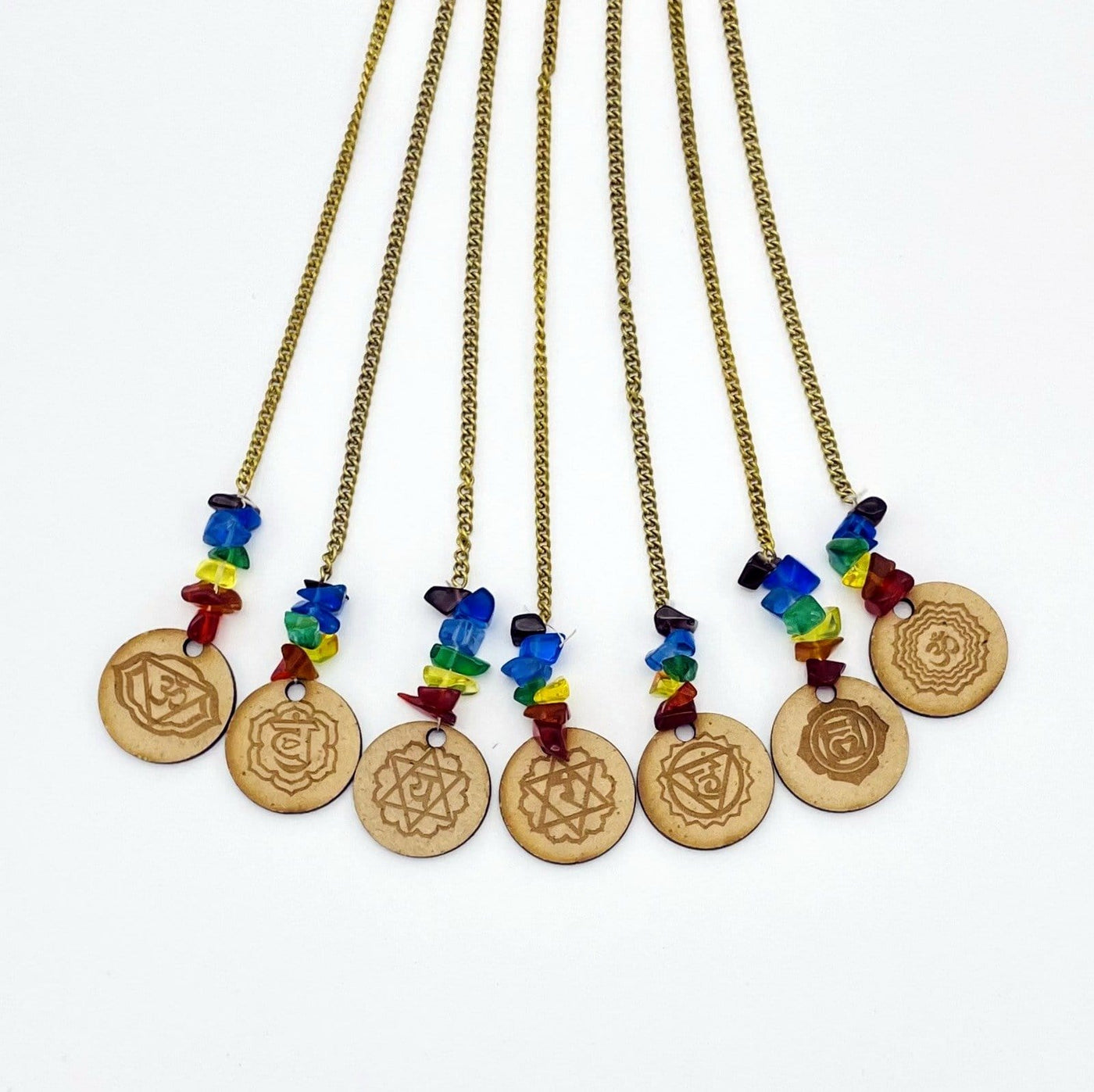 Mini engraved wood circles Each decorated with chakra colored tumbled glass accents on a white background.