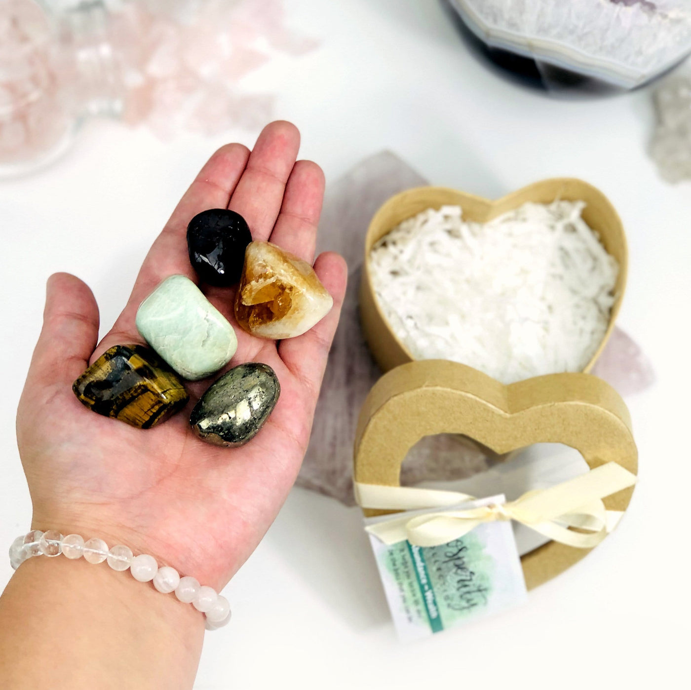 hand holding up tigers eye, citrine, aventurine, garnet, and pyrite with prosperity heart box blurred in the background with decorations