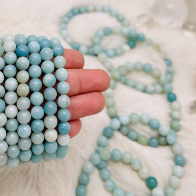 Multiple amazonite bead bracelets being held, with more in the back ground.