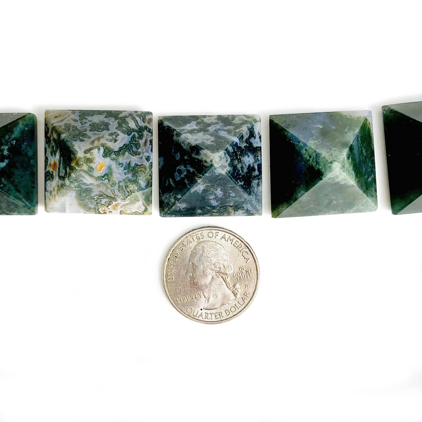 Moss agate assorted pyramids on a white background with a quarter next to it.  The pyramids are 1 inch and about the size of the quarter.