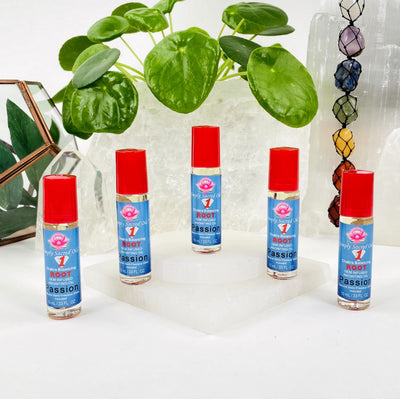5 Root Chakra Balancing Oils arranged with other crystals and plants in the background