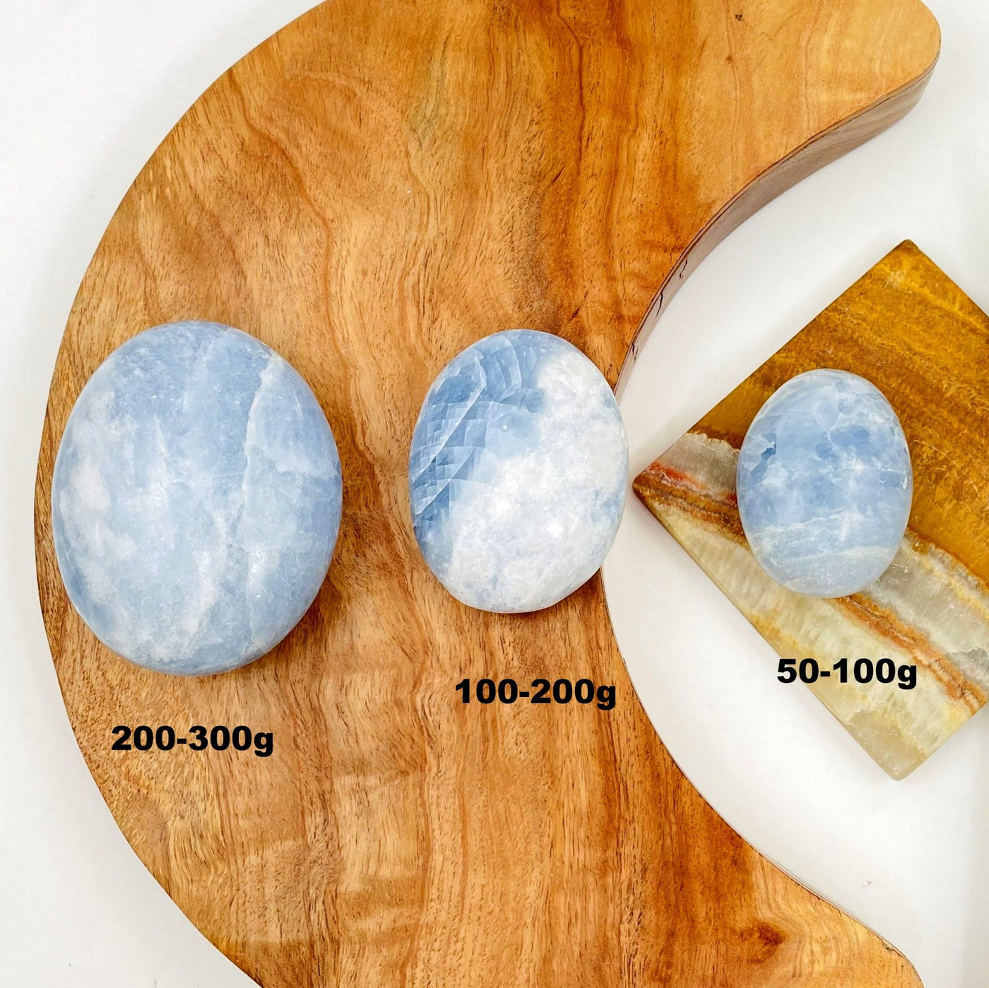 3 sizes of blue calcite palm stones on a piece of wood