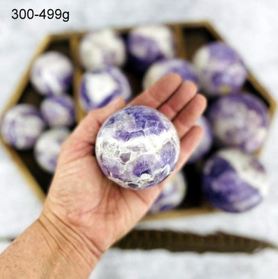 Chevron Amethyst Polished Sphere of 300-499g displayed in palm of woman's hand.