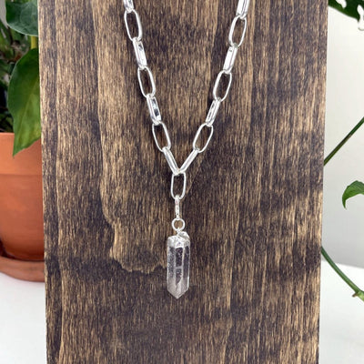 a crystal point charm on the silver charm necklace on a stand up close