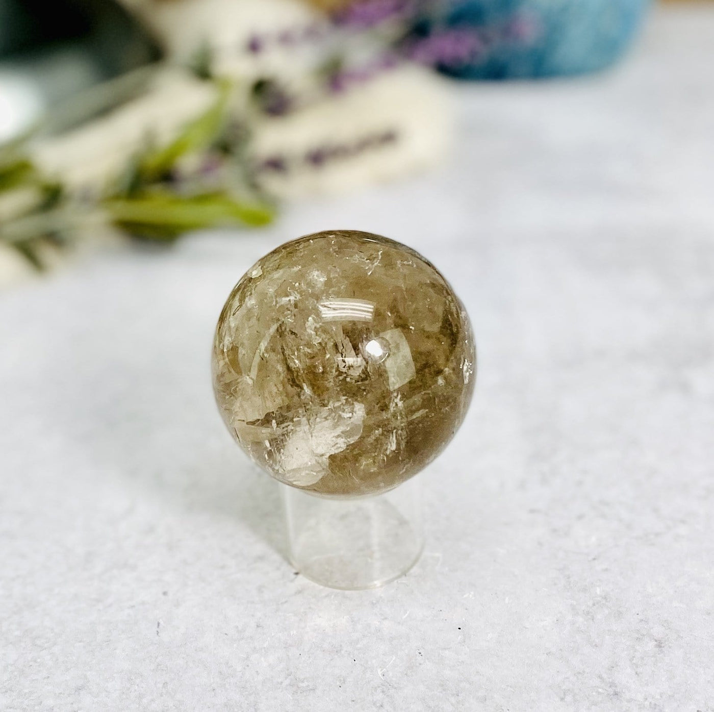 smokey quartz polished sphere on clear stand in front of backdrop for details