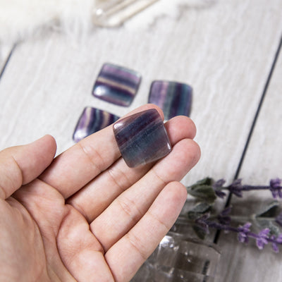 hand holding up rainbow fluorite square cabochon with others blurred in the background