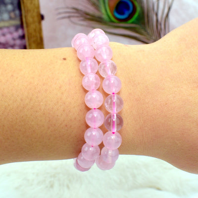 Wrist wearing 2 Rose Quartz Round Bead Bracelets with decorations blurred in the background