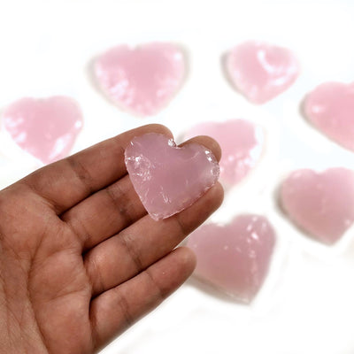 Hand holding up heart shaped rose quartz with others blurred in the background