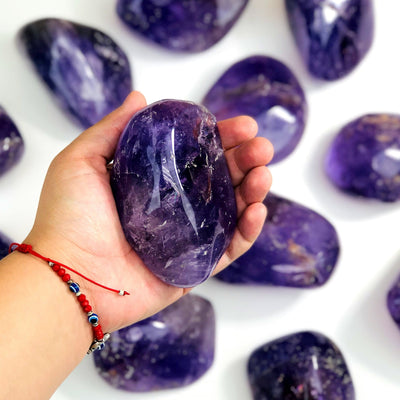 hand holding up amethyst tumbled stone with others on white background