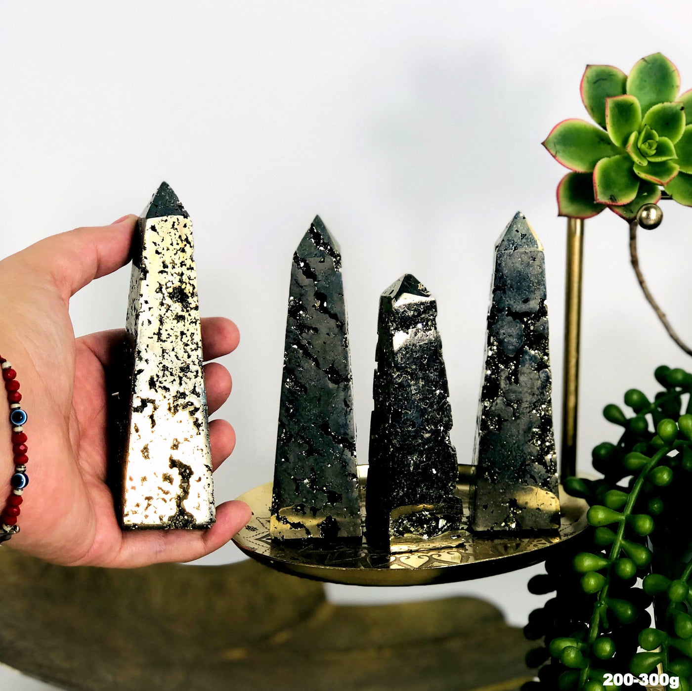 Four assorted pyrite obelisk towers on a gold background and one is in a woman's hand.