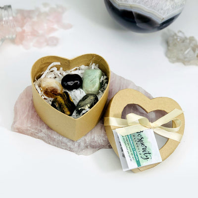 opened prosperity heart box with crystals inside on top of a rose quartz slab with other crystals blurred in the background