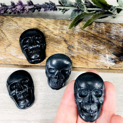 hand holding obsidian skull cabochon with 3 others in the background with decorations