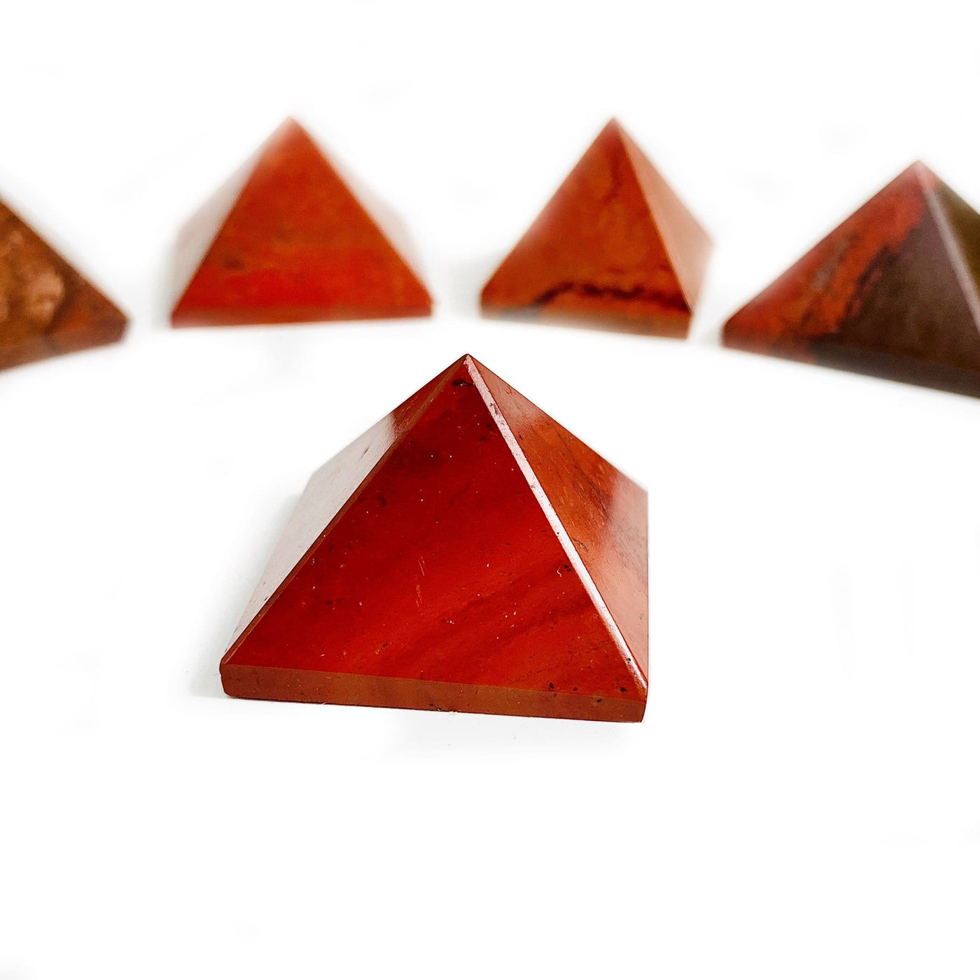 1 Red Jasper Pyramid up close with 4 others blurred on white background