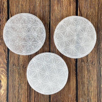 overhead close up of three selenite round plates engraved with flower of life for engraving details and possible variations