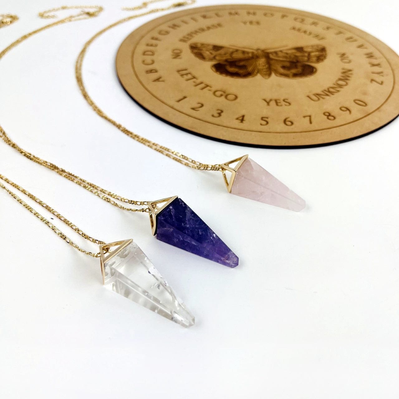 Rose Quartz Amethyst and Crystal Quartz Pendulum Necklaces in gold on a table