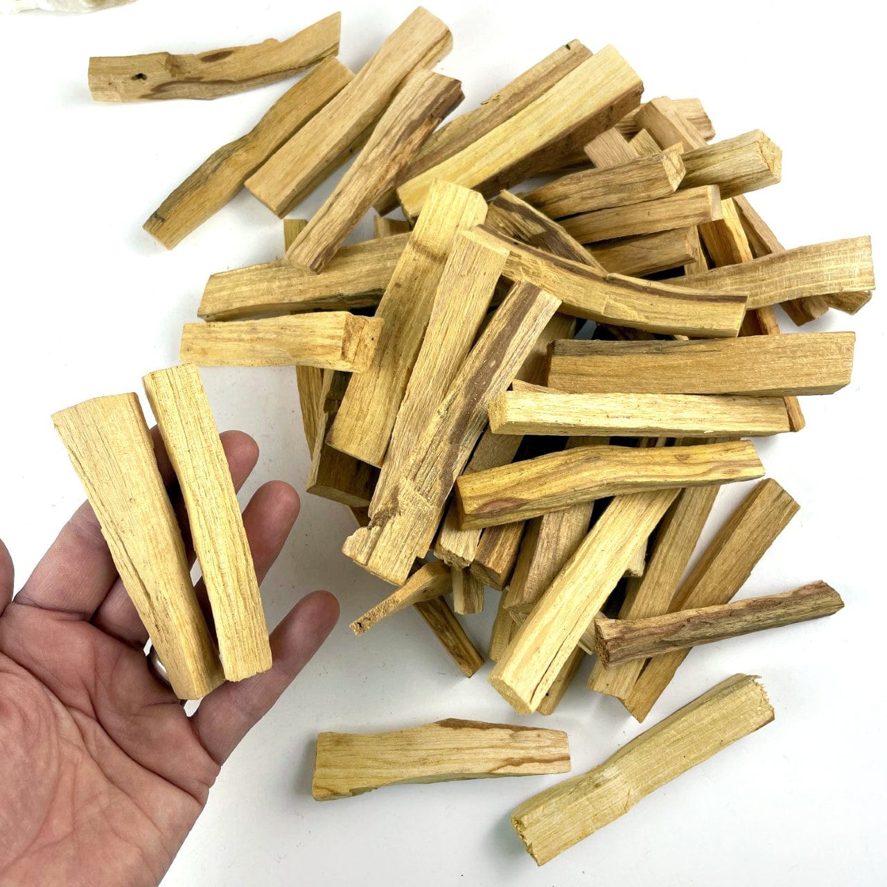 A pile of palo santo sticks and two held in a hand.