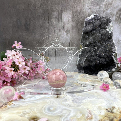 A front facing Acrylic Sphere Holder Crescent Moons - Six Pointed Star in an alter surrounded with flowers and crystals.