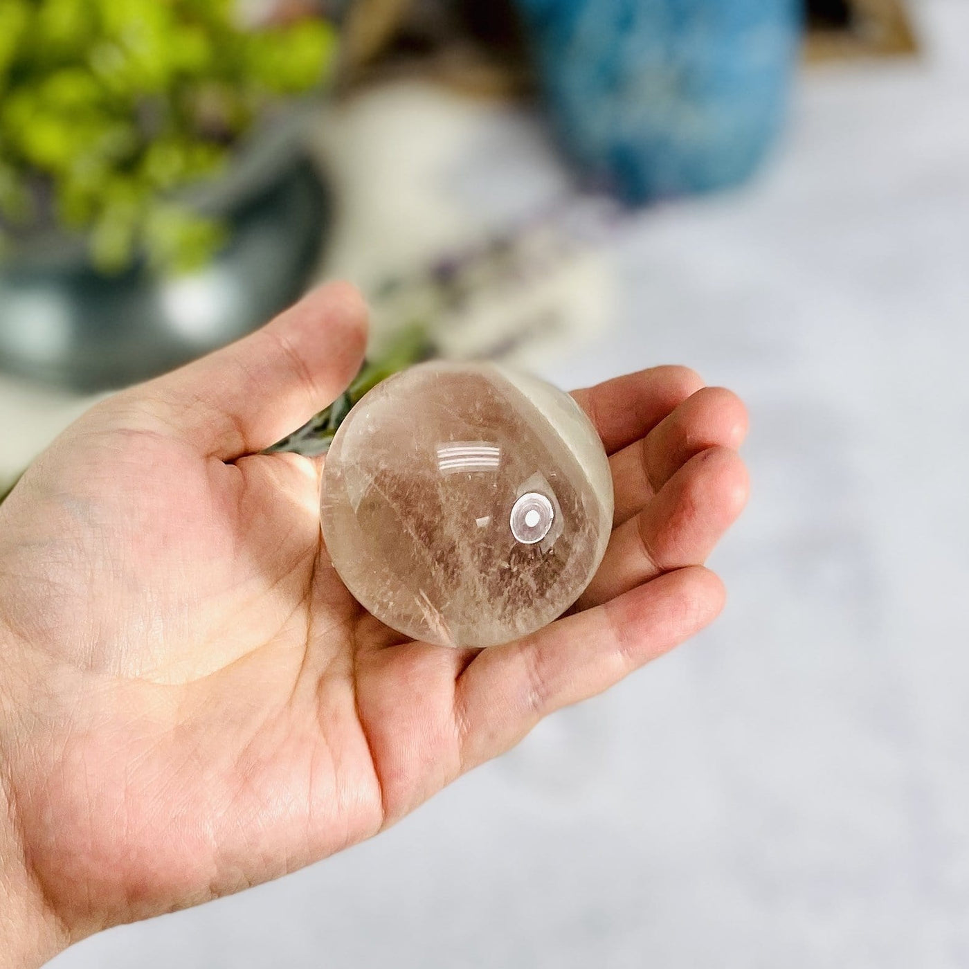 hand holding up Crystal Quartz Polished Sphere with decorations blurred in the background