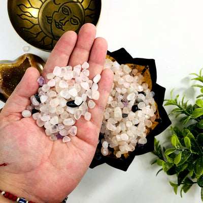 Rose quartz chips in a lotus bowl, a few other stones are in the mix.  A hand is holding some chips above the bowl