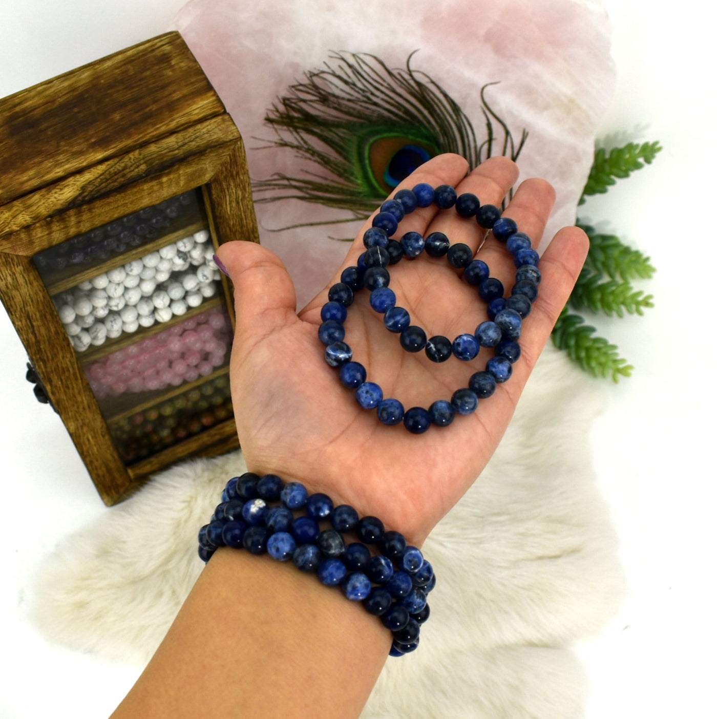 two sodalite round bead bracelets in hand and three more on wrist for size reference and possible variations