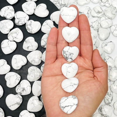 hand holding up 6 howlite hearts with more in the background