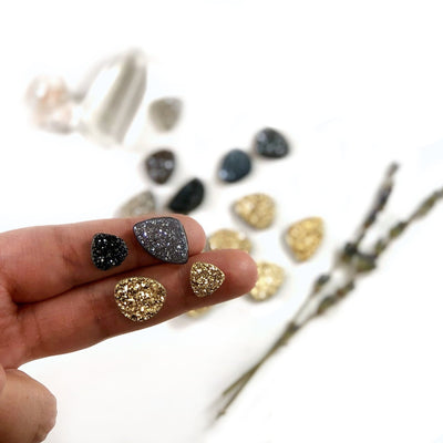 hand holding up 4 black diamond and gold druzy cabochons with more blurred in the background