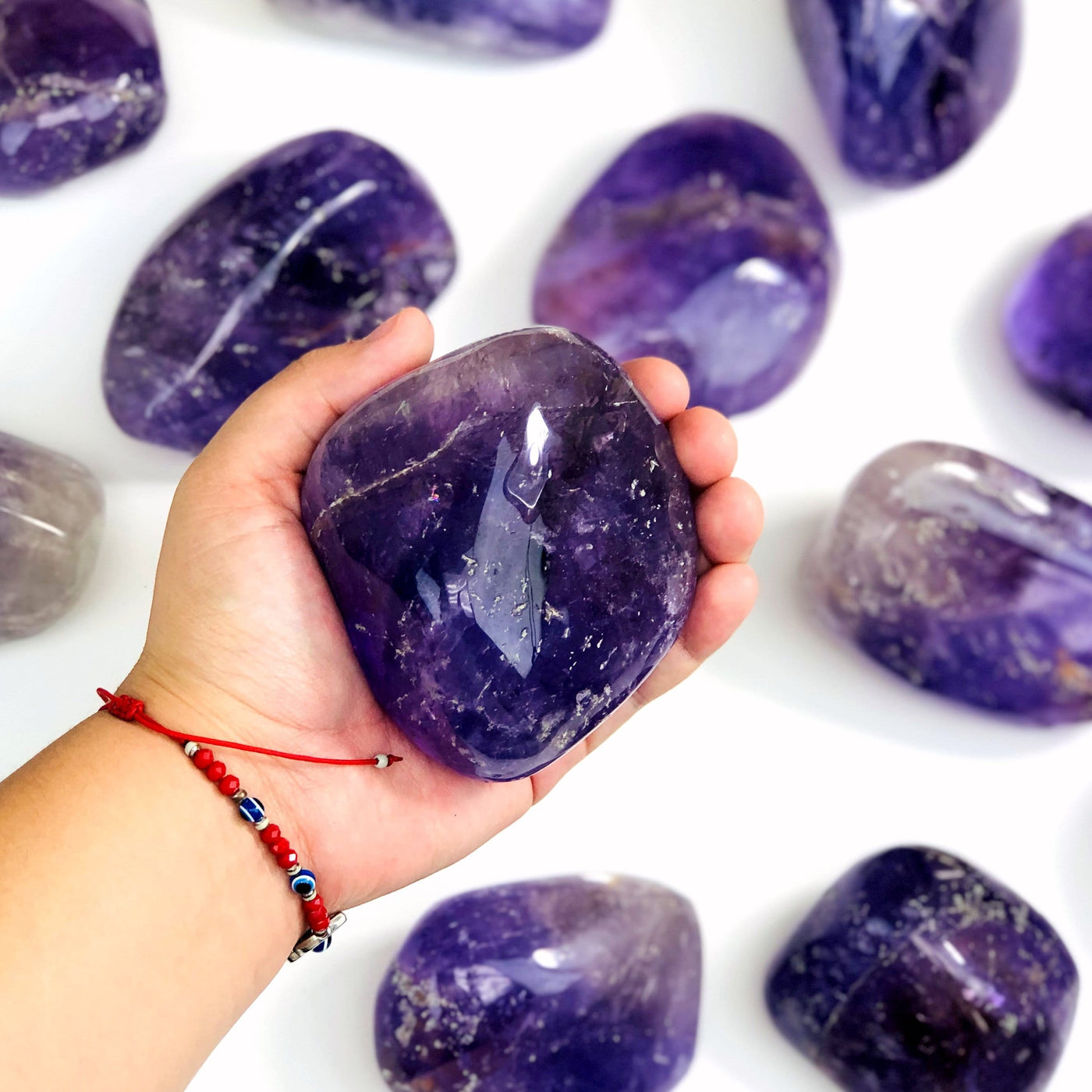 hand holding up amethyst tumbled stone with others on white background