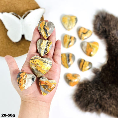 hand holding up 5 20-50g bumblebee jasper hearts with 7 others burred with decorations in the background