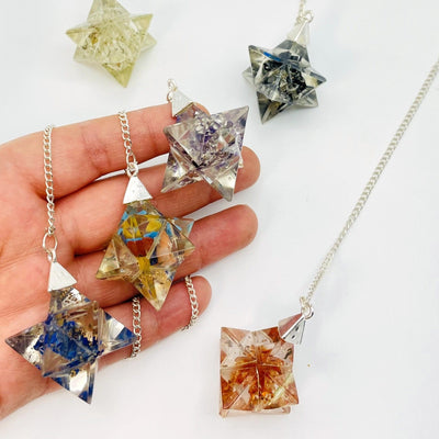 hand holding up 3 orgone merkaba star pendulums with 3 others on white background