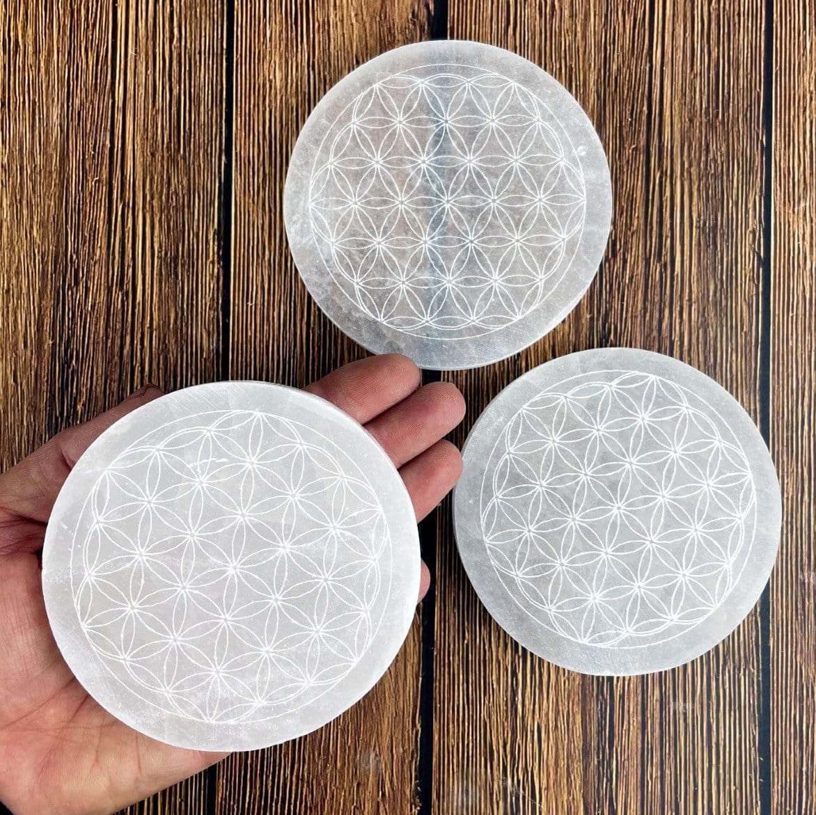selenite round plate engraved with flower of life in hand for size reference with two others in background display for possible variations