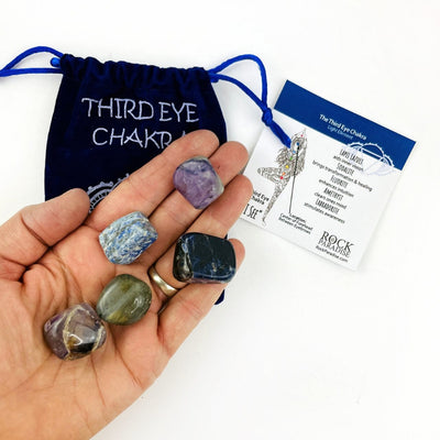 The Third Eye Chakra Set of tumbled stones in a hand, with the information card and pouch behind