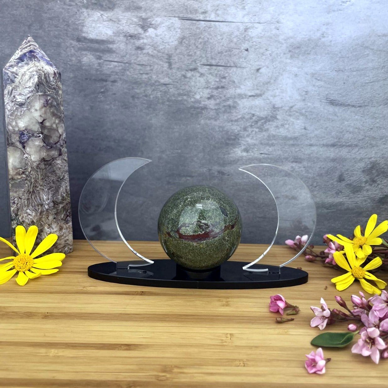 Acrylic Sphere Holder Crescent Moons is shown front facing holding a sphere in an alter surrounded by flowers.