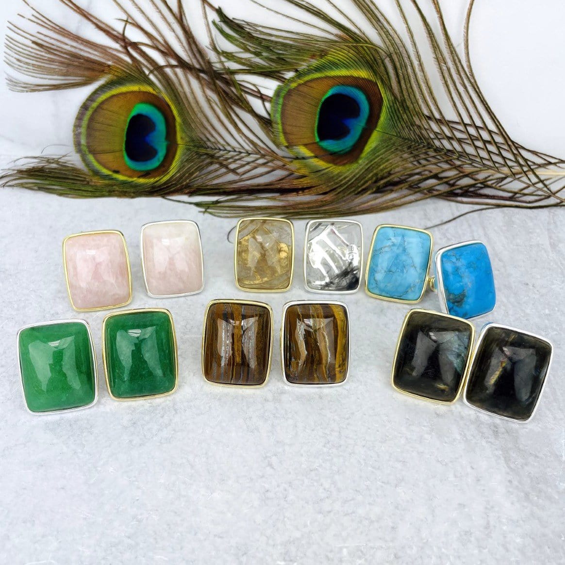 various stone rings in gold and silver in front of peacock feather