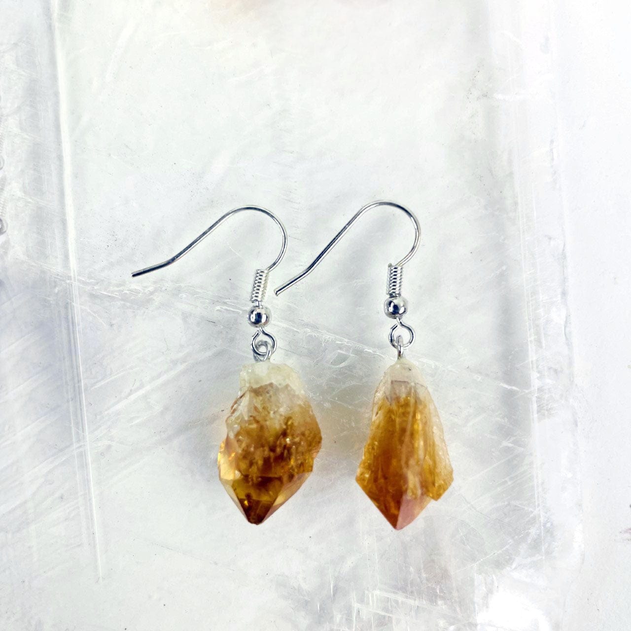 Close up of citrine point earrings in silver plated on a selenite slab