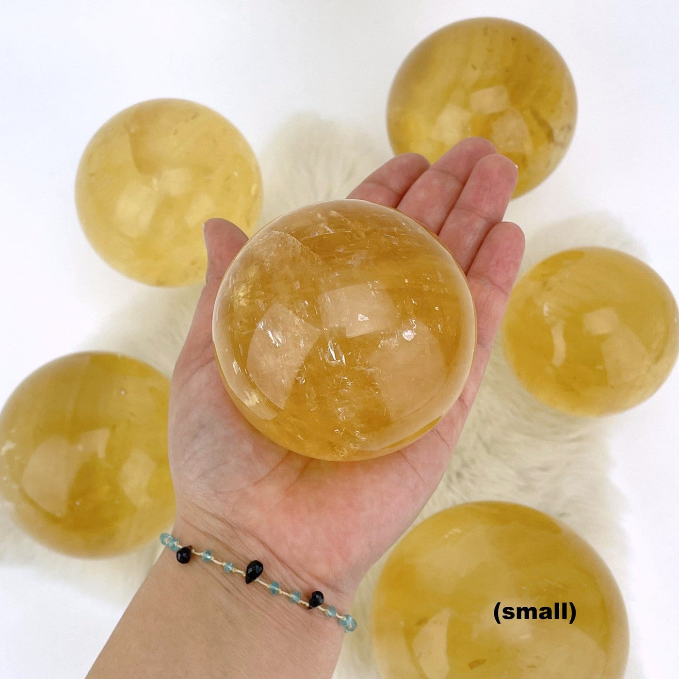 hand holding up small Honey Calcite Polished Sphere with others in the background