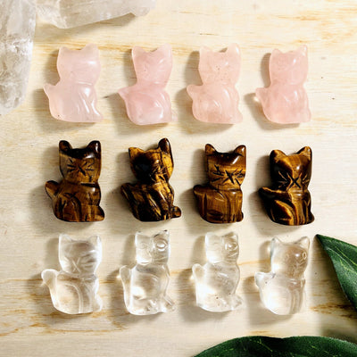 12 cats on a wood background. top 4 are rose quartz, middle 4 are tiger eye, bottom 4 are crystal quartz 