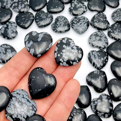 close up of snowflake obsidian hearts in hand for details with many others filling the background