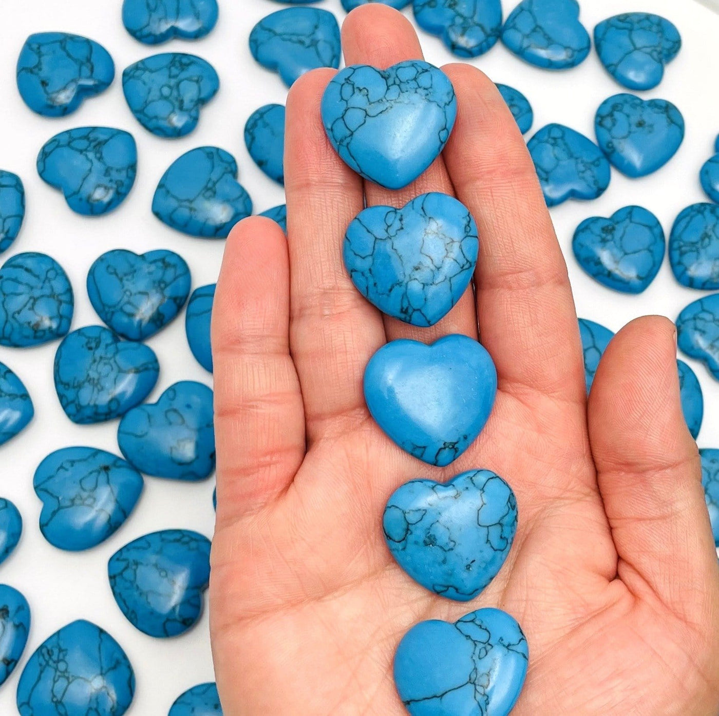 Turquoise Howlite Heartsin a hand for size reference and a lot of others behind on a table