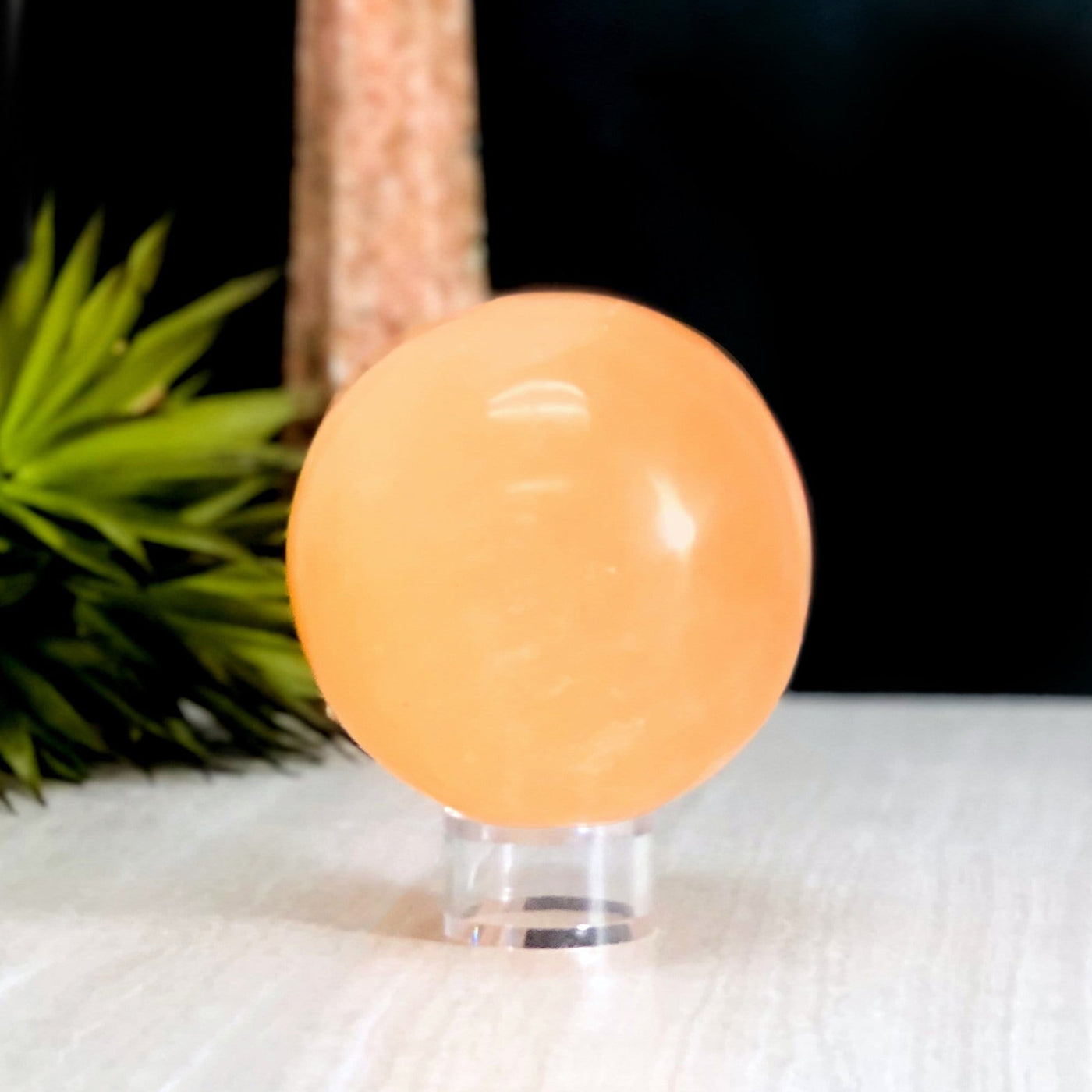Orange Selenite Sphere on stand with decorations in the background