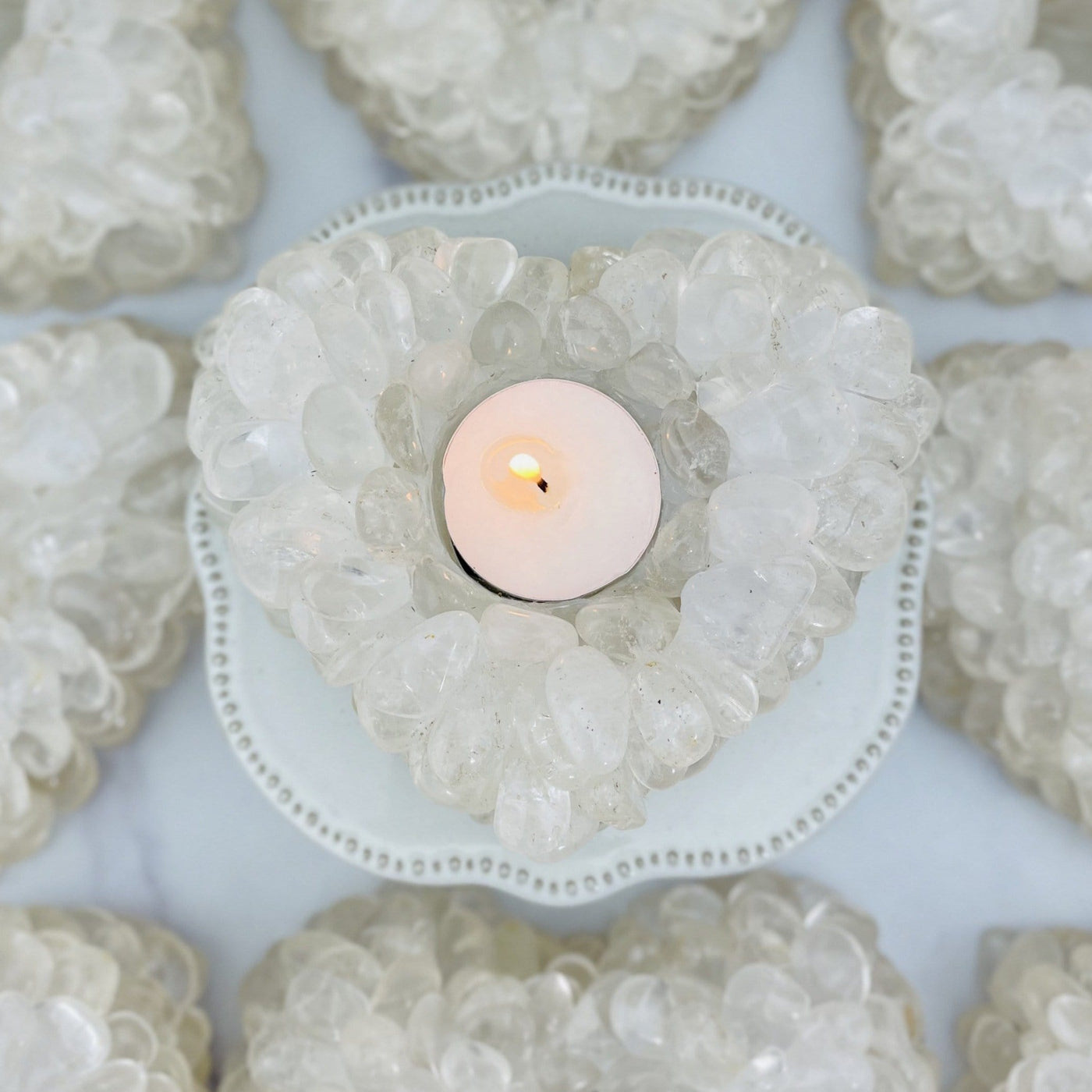 Heart shaped candle holder that is made with crystal quartz tumbled stones that are glued together. In this photo it is shown with a tealight lit candle and more in the background.