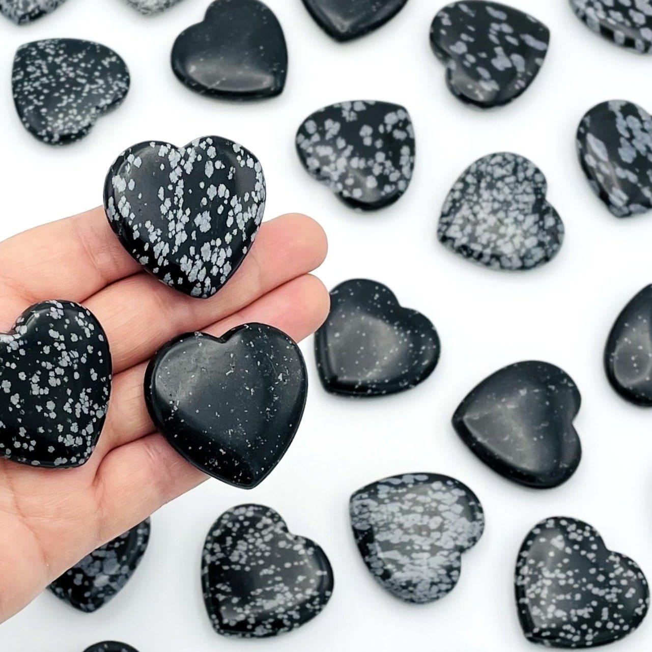 three snowflake obsidian hearts in hand for size reference with many others in background for possible variations