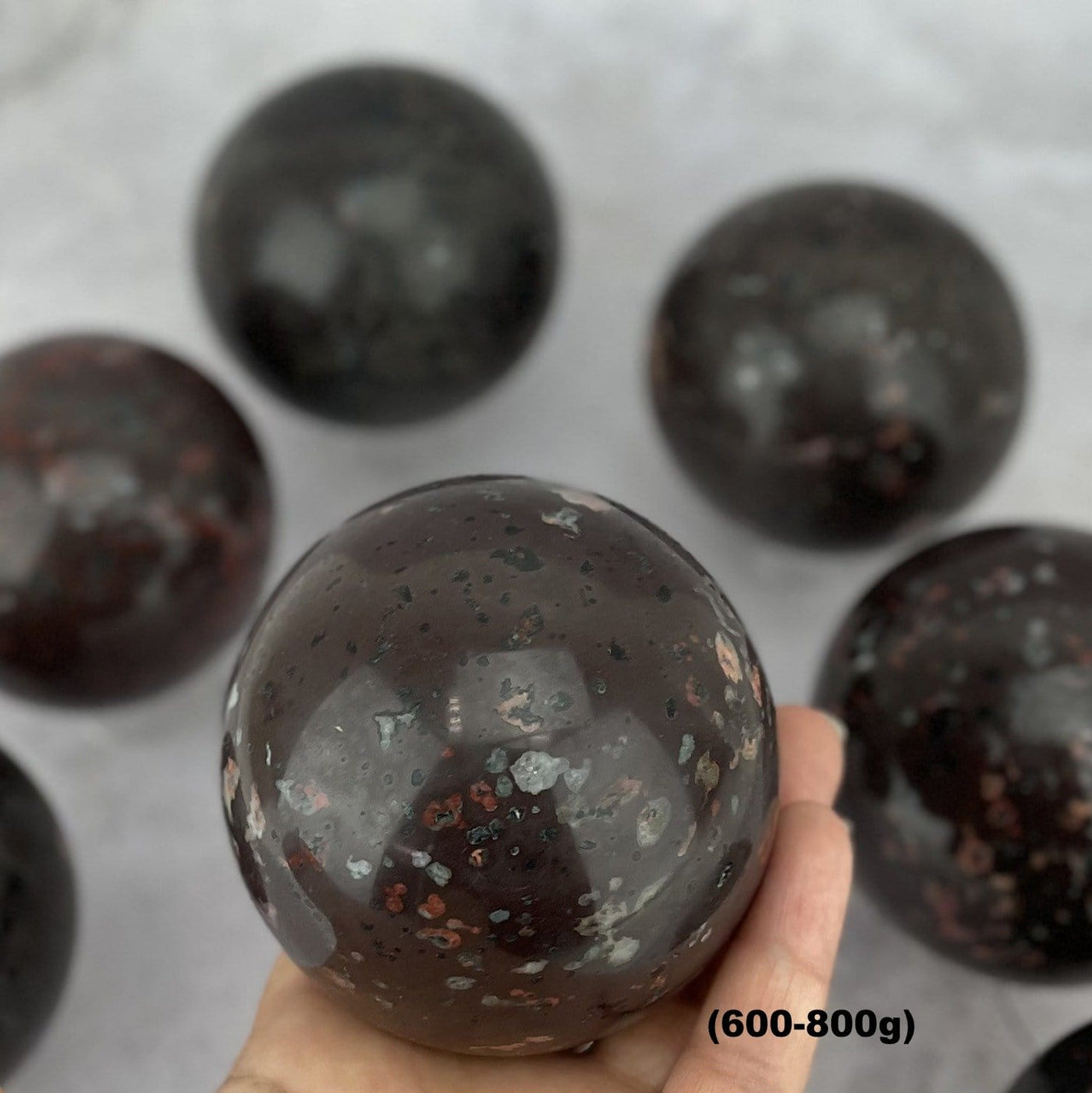 hand holding up 600-800g plum blossom jasper stone sphere with other blurred in the background