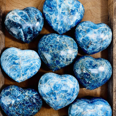 Blue Apatite Polished Hearts displayed in wooden tray showing the various color shades formations and natural inclusions