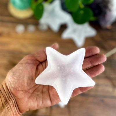 hand holding up star selenite dish with decorations blurred in the background