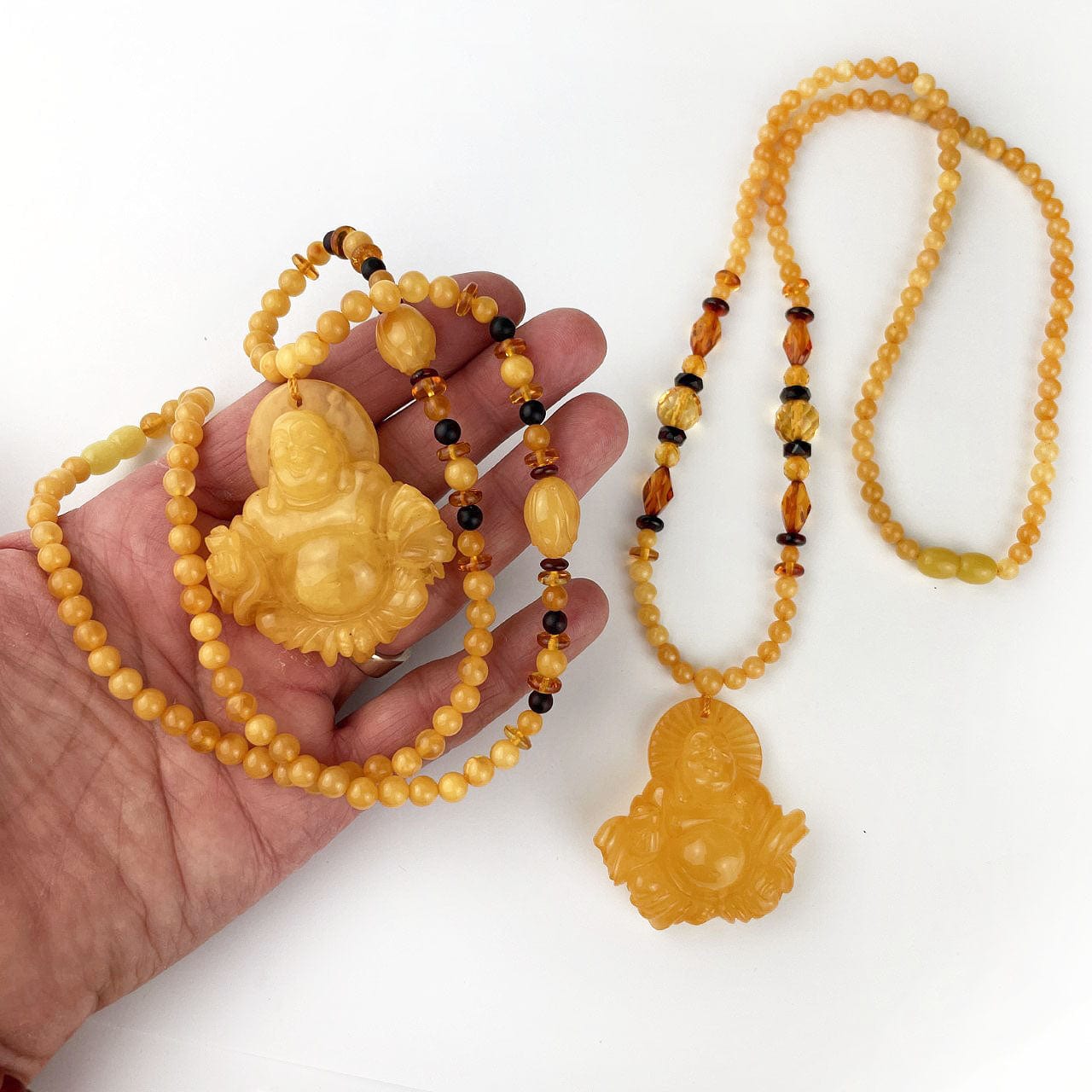 Amber Beaded Necklaces with Carved Buddha Pendants, shown here with one in a hand.