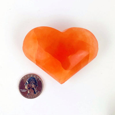 A Orange Selenite Puffy Heart Around a quarter for sizing 